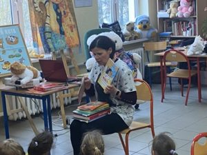 Ciemnowłosa, siedząca kobieta trzyma książkę w ręce.