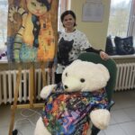 Ciemnowłosa kobieta pozuje z dużym pluszakiem i portretem kota.