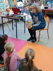 Blondwłosa kobieta pokazuje dzieciom książkę.