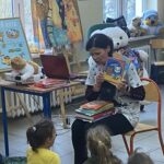 Ciemnowłosa kobieta pokazuje książkę grupie dzieci.