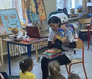 Ciemnowłosa kobieta pokazuje książkę grupie dzieci.