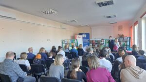 Sala wypełniona gośćmi uroczystości, Do zebranych zwracają się dwie kobiety w strojach regionalnych.