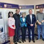 Kobiety w czerwonej spódnicy i zielonym żakiecie, dwaj mężczyźni w garniturach i mężczyzna w golfie pozują do zdjęcia.