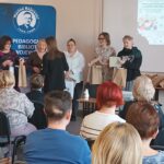 Sala audytoryjna pełna słuchaczy, dwie kobiety wręczają nagrodę 4 kobietom.