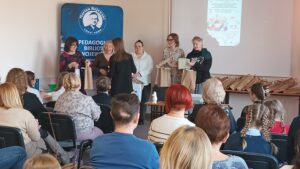 Sala audytoryjna pełna słuchaczy, dwie kobiety wręczają nagrodę 4 kobietom.