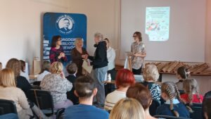 Sala audytoryjna pełna słuchaczy, dwie kobiety wręczają nagrody 3 kobietom.