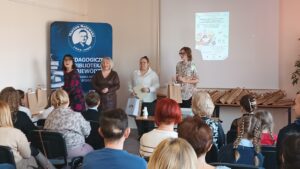 Sala audytoryjna pełna słuchaczy, jako mówcy stoją 4 kobiety.