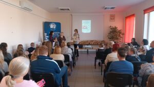 Sala audytoryjna pełna słuchaczy, jako mówcy stoją 3 kobiety.