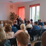 Sala audytoryjna pełna słuchaczy, jako mówca stoi kobieta w brązowej sukience.