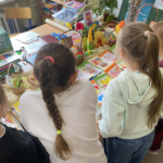 Dzieci stojące tyłem przy stoliku z kartkami z kolorawnek.