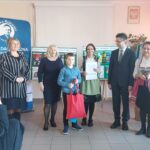 Laureat konkursu z torbą prezentową w otoczeniu organizatorów.