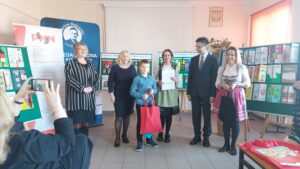 Laureat konkursu z torbą prezentową w otoczeniu organizatorów.