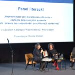 Dwoje panelistów i prowadząca dyskusję przed dużym ekranem.