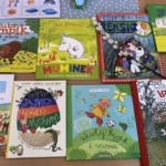 Zdjęcie kilku książek rozłożonych na biurku z gałązką bazi.