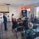 Kobieta w czerwonej spódnicy i mężczyzna w garniturze stoją przed publicznością,