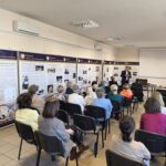 Sala audytoryjna pełna ludzi. Przodem do nich stoi mężczyzna.