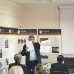 Mężczyzna w garniturze stoi w sali przed publicznością.