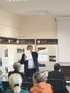 Mężczyzna w garniturze stoi w sali przed publicznością.