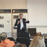 Mężczyzna w garniturze stoi w sali przed publicznością.