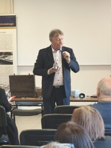 Mężczyzna w garniturze stoi w sali przed publicznością.