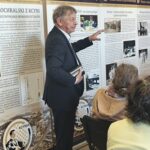 Mężczyzna w garniturze pokazuje na elementy wystawy.