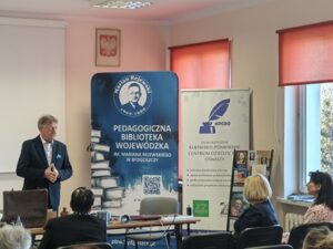 Mężczyzna na przedzie sali, w pierwszych rzędach siedzą kobiety.