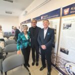 Dwóch mężczyzn w garniturach i kobieta w zielonym żakiecie.