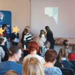 3 kobiety wręczają nagrody dzieciom. Twarze dzieci zasłonięte gwiazdkami.