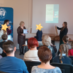 3 kobiety wręczają nagrody dzieciom. Twarze dzieci zasłonięte gwiazdkami.