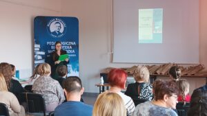 Kobieta w zielonej sukience stoi przed widownią i czyta z zielonej podkładki.