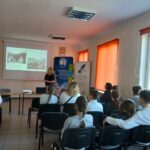 Grupa młodzieży siedzą w sali, przodem do prezentacji.