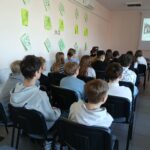 Grupa młodzieży, tyłem do obiektywu, siedzi na krzesłach.