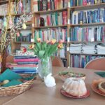 Mazurek, bukiet kwiatów i stos książek na stole.