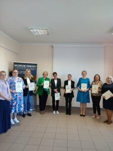 W półkolu stoi grupa osób, trzymając kartki.