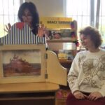 Dwie kobiety w otoczeniu teatrzyku kamishibai.