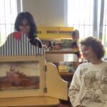 Teatrzyk kamishibai na stole - dwie kobiety obok.