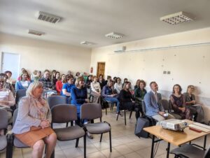 Fotografia sporej grupy osób siedzącej na krzesłach.