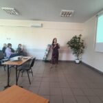 Kobieta w sukience w kwiaty przemawia do publiczności.