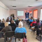 Kobieta w czarnym swetrze występuję przed publicznością.