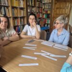 Kilka kobiet siedzi wokół stołu. Na stole są kartki papieru.