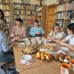 Na stole są przekąski i kubki, wokół stołu siedzi grupa kobiet.