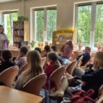 Grupa dzieci z opiekunką na zajęciach edukacyjnych w czytelni.