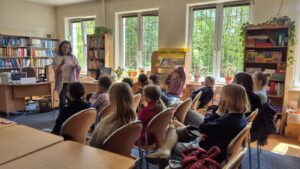 Grupa dzieci z opiekunką na zajęciach edukacyjnych w czytelni.