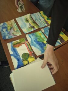 Dłoń chwyta kartkę papieru, obok 6 ilustracji akwarelowych.