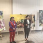 3 kobiety stoją na tle obrazów na sztalugach.