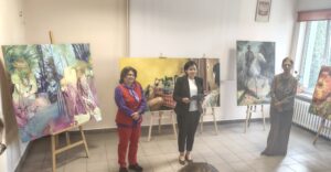 3 kobiety stoją na tle obrazów na sztalugach.