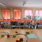Grupa dzieci pozuje do zdjęcia, trzymając w rękach niebieski brystol z kolorowymi wagonami.