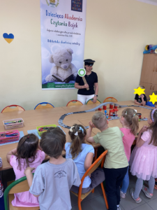 Wokół stołu z kolejką elektryczną stoi grupka dzieci i kobieta.