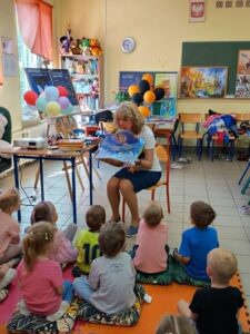 Kobieta prezentuje małym dzieciom książkę przestrzenną.