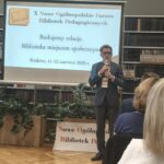 Mężczyzna w garniturze i okularach mówi do mikrofonu.